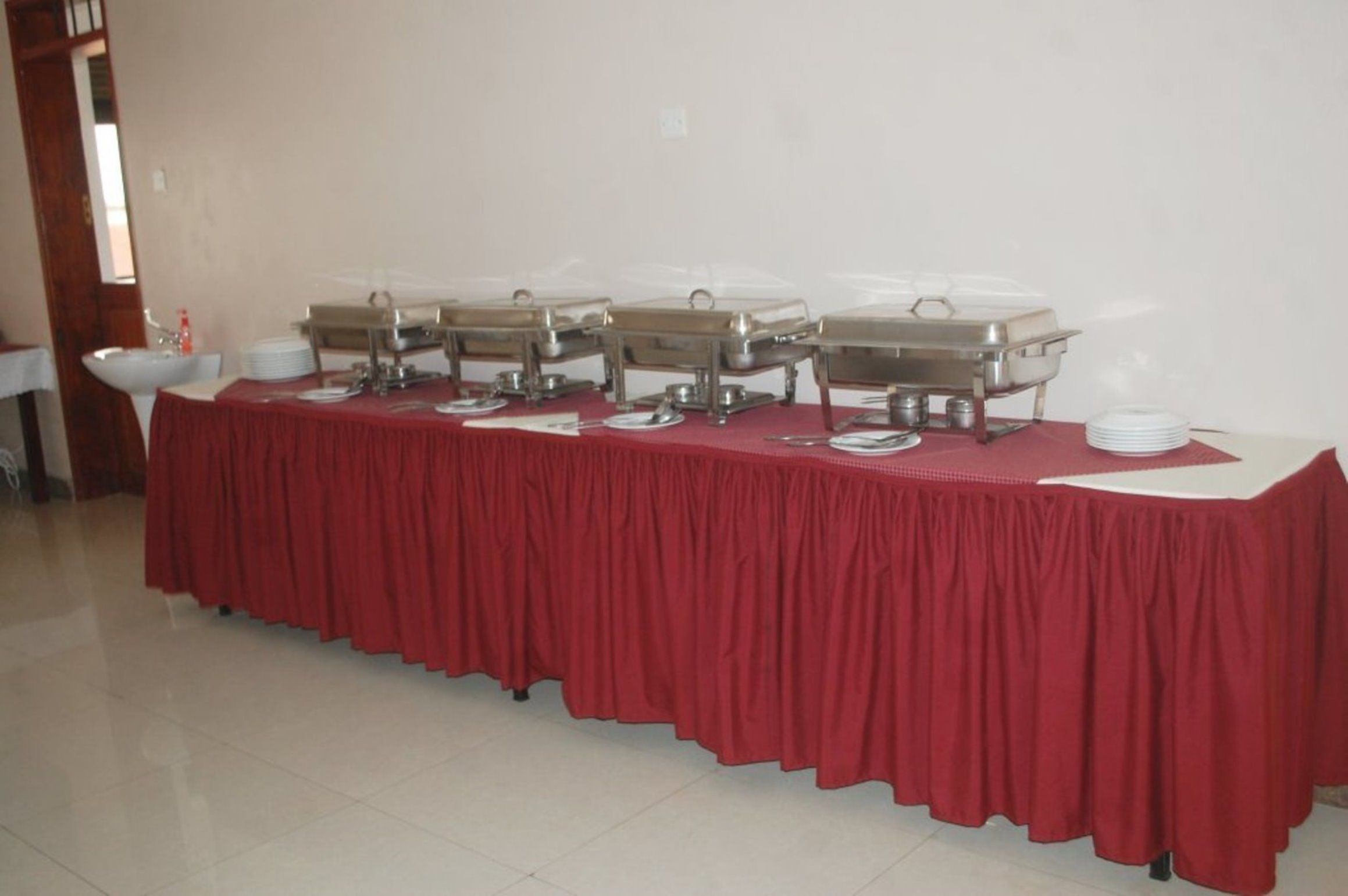 A buffet table with multiple chafing dishes and serving utensils, set against a plain wall.