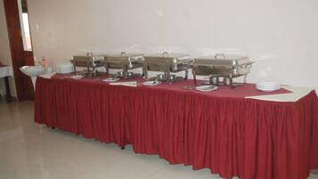 A buffet table with multiple chafing dishes and serving utensils, set against a plain wall.
