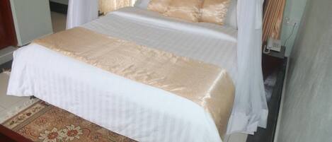 A neatly made bed with a white and gold bedspread, a wooden headboard, and a canopy.