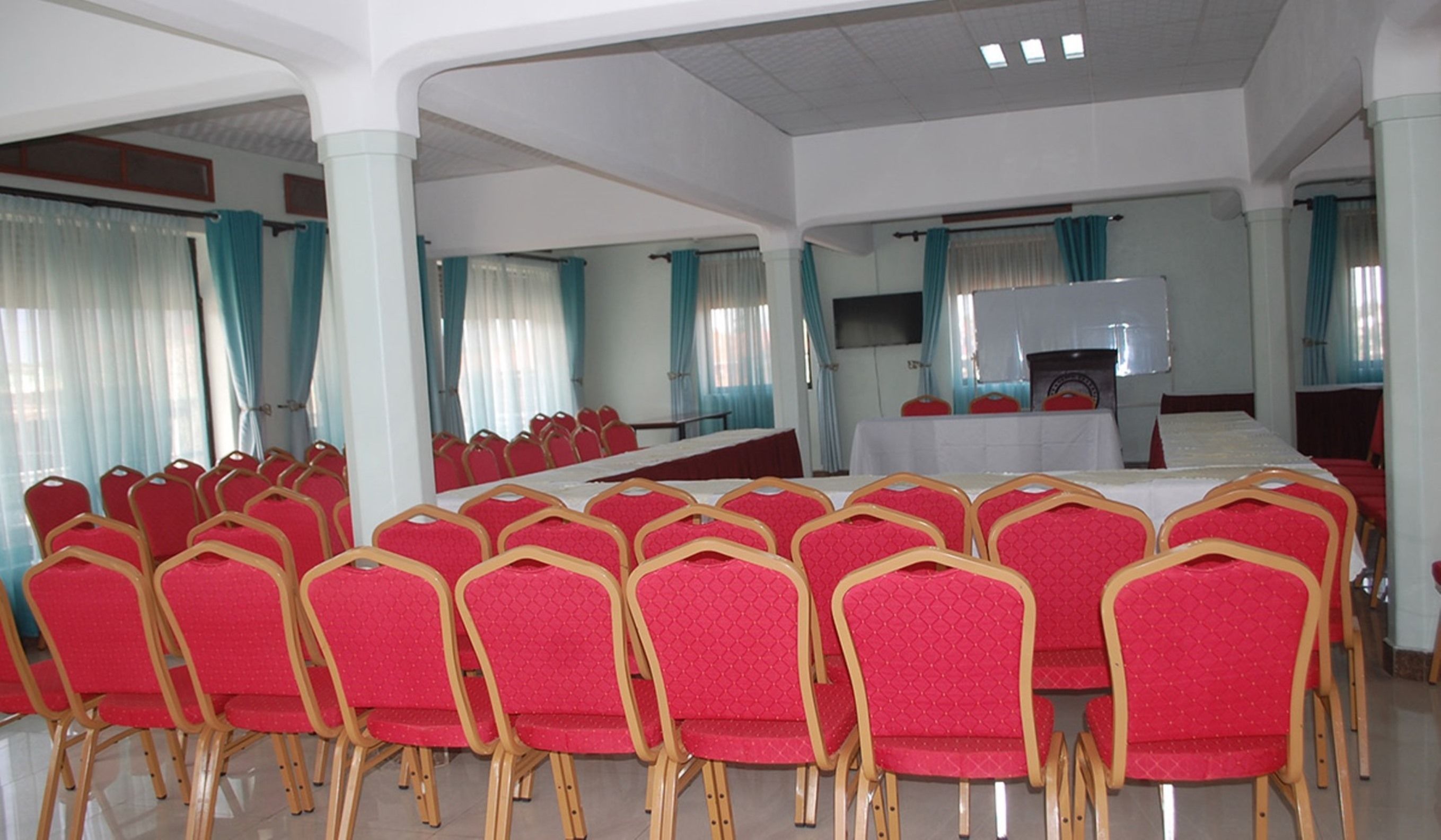 A conference room with rows of red chairs, a long table, and a television screen.