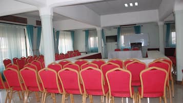 A conference room with rows of red chairs, a long table, and a television screen.