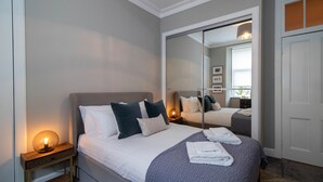 A neatly arranged bedroom with a bed, bedside table, and a large mirror reflecting the room. - Nairn Apartment - West End close to University (Glasgow)