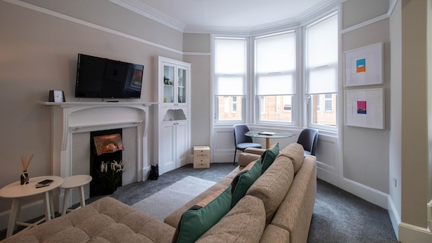 A living room with a fireplace, a television, a sofa, and a dining area. - Nairn Apartment - West End close to University (Glasgow)
