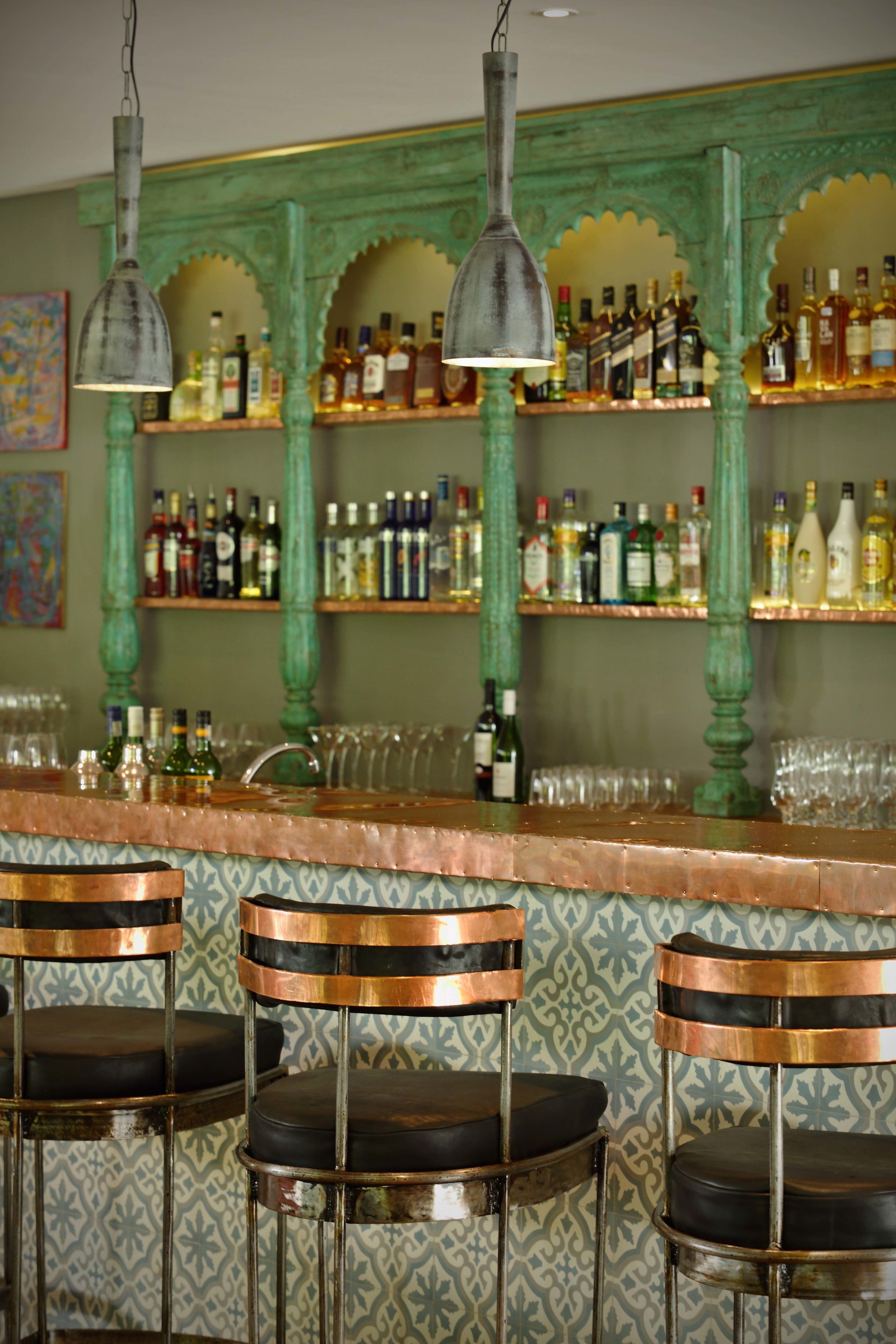A bar area with three stools, shelves with bottles, and hanging lights.