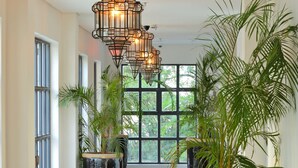A hallway with large potted plants, a checkered floor, and hanging pendant lights. - Latitude 0 Degrees (Kampala)