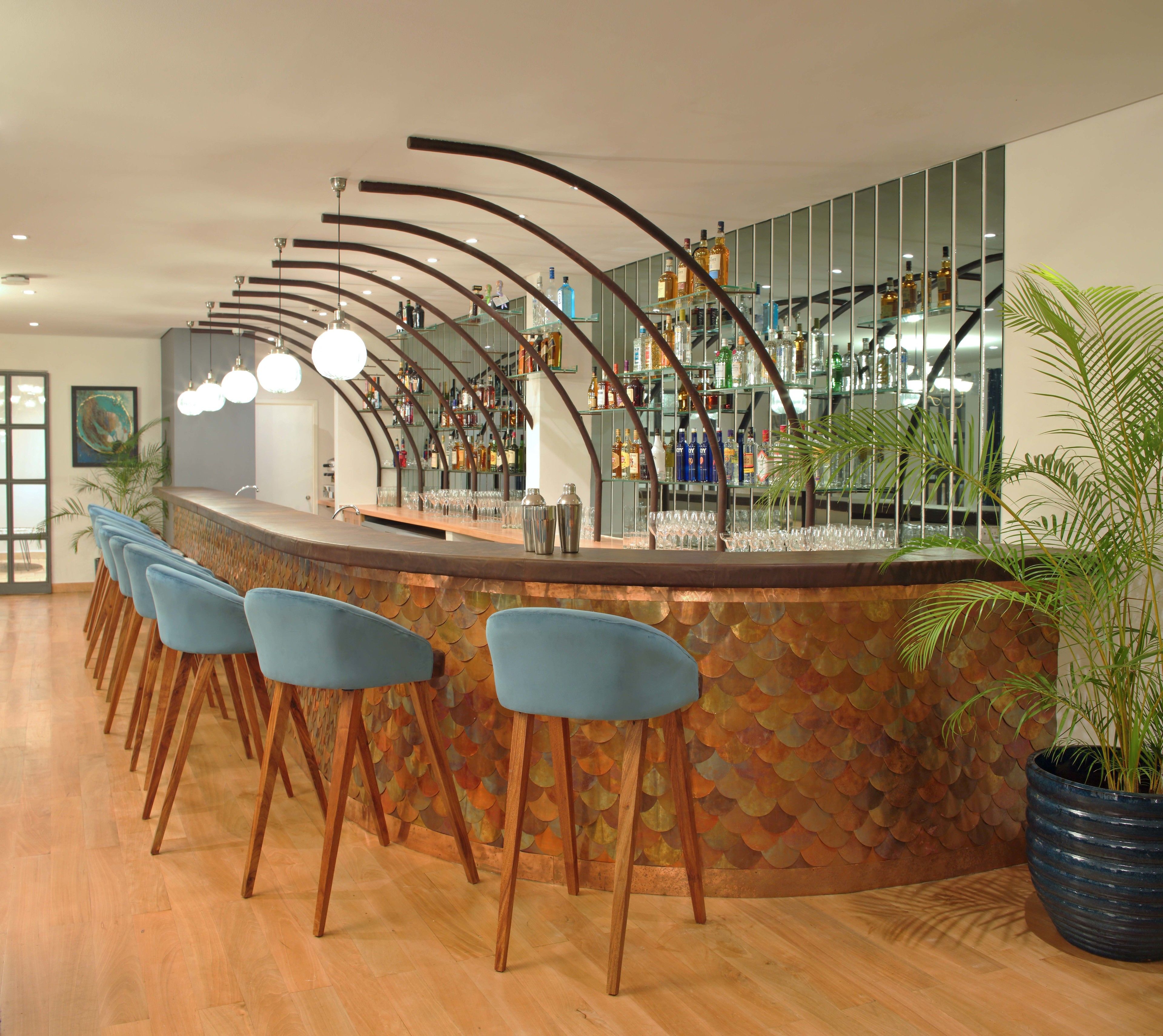A bar area with a curved counter, blue bar stools, and a variety of bottles and glasses.