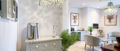 A modern living room with a patterned console table, a potted plant, and a dining area with a glass table and chairs.