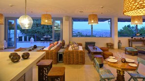 A spacious dining area with wicker furniture, large windows offering a view of the landscape, and hanging lamps. - Latitude 0 Degrees (Kampala)