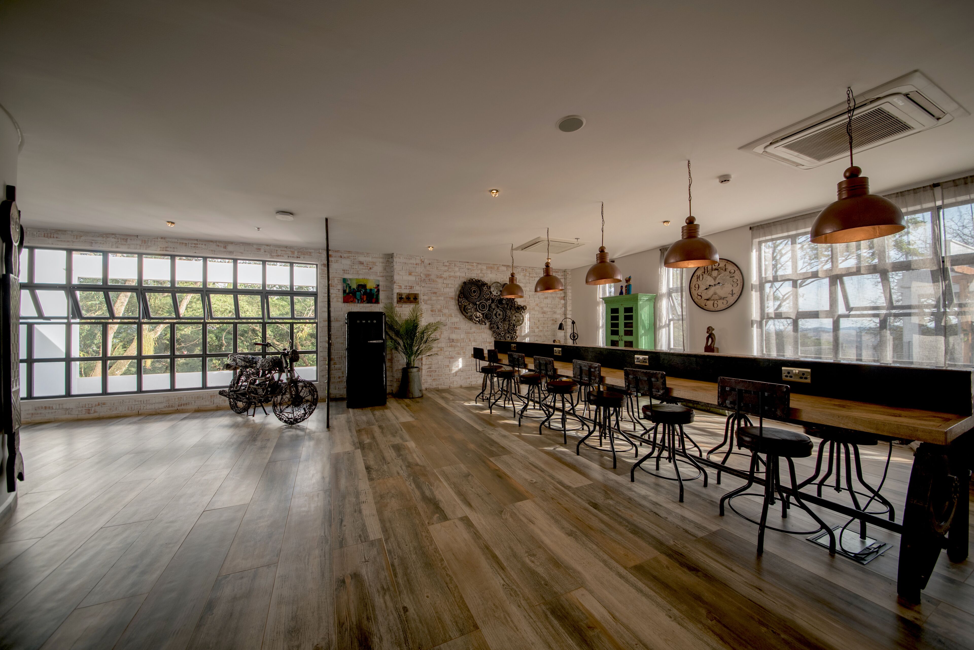 Une pièce spacieuse avec un long comptoir en bois, de nombreux tabourets de bar et de grandes fenêtres offrant une vue sur la verdure environnante.