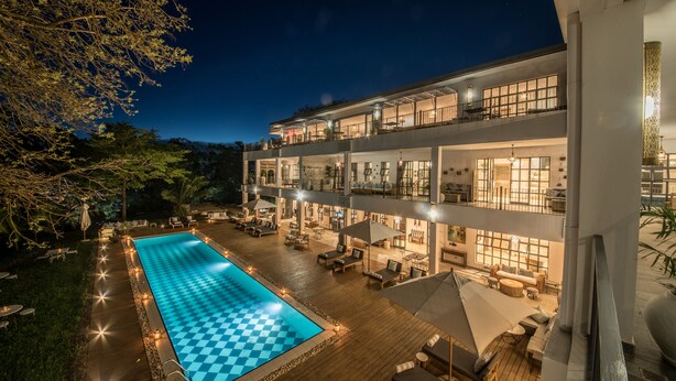 A multi-story hotel with a swimming pool, outdoor seating, and a well-lit terrace. - Latitude 0 Degrees (Kampala)