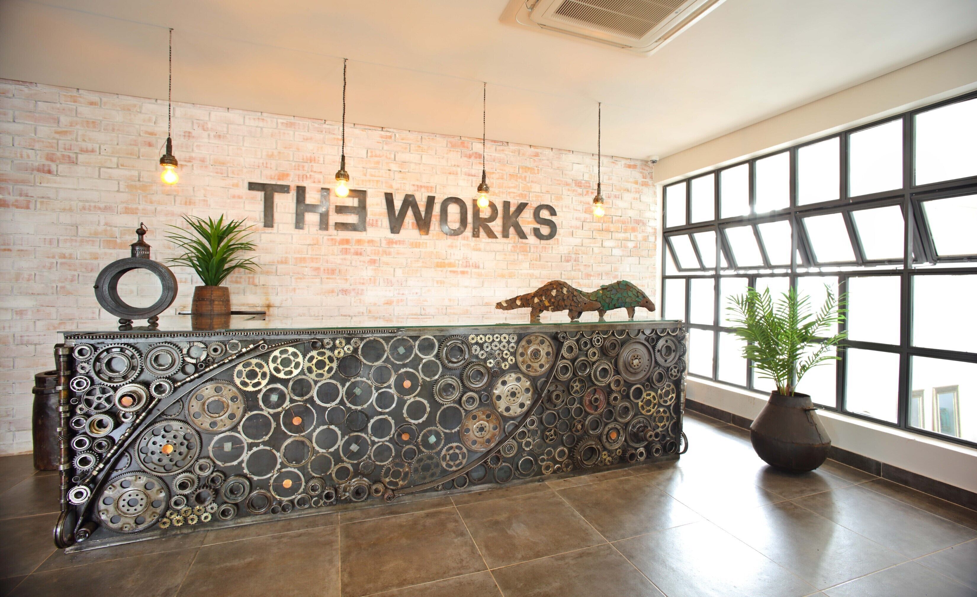 A reception desk with a brick wall background, a sign reading "THE WORKS", and a large window to the right.