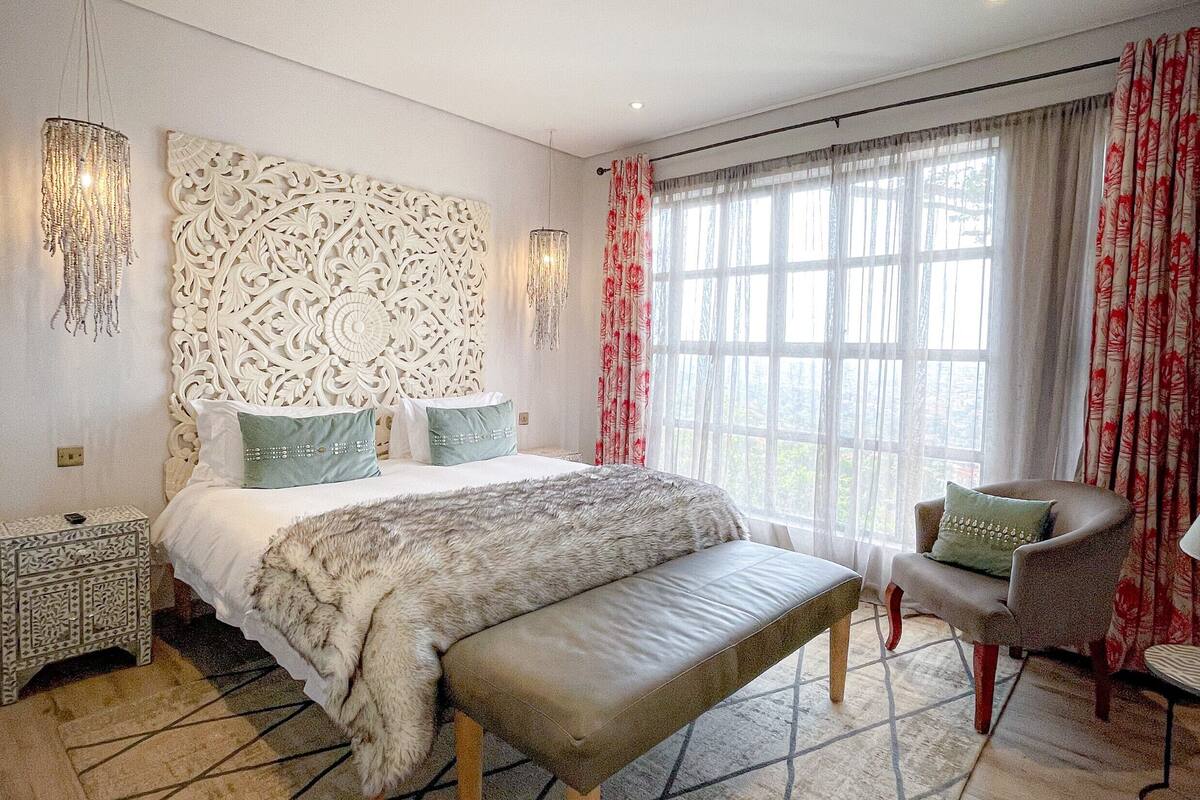 A modern bedroom with a large bed, a bench, a chair, and a patterned rug.