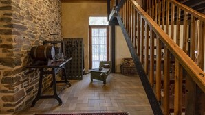 Un interior rústico con una escalera de madera, paredes de piedra y una mesa de madera tradicional con un barril.