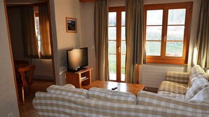 A cozy living room with a checkered sofa, a television on a wooden stand, and a view of the outdoors through large windows. - Jacqueline 1 by Interhome (Gstaad)