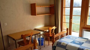 A room with two beds, a desk, and a chair. There is a window with a view of greenery outside. - Jacqueline 1 by Interhome (Gstaad)