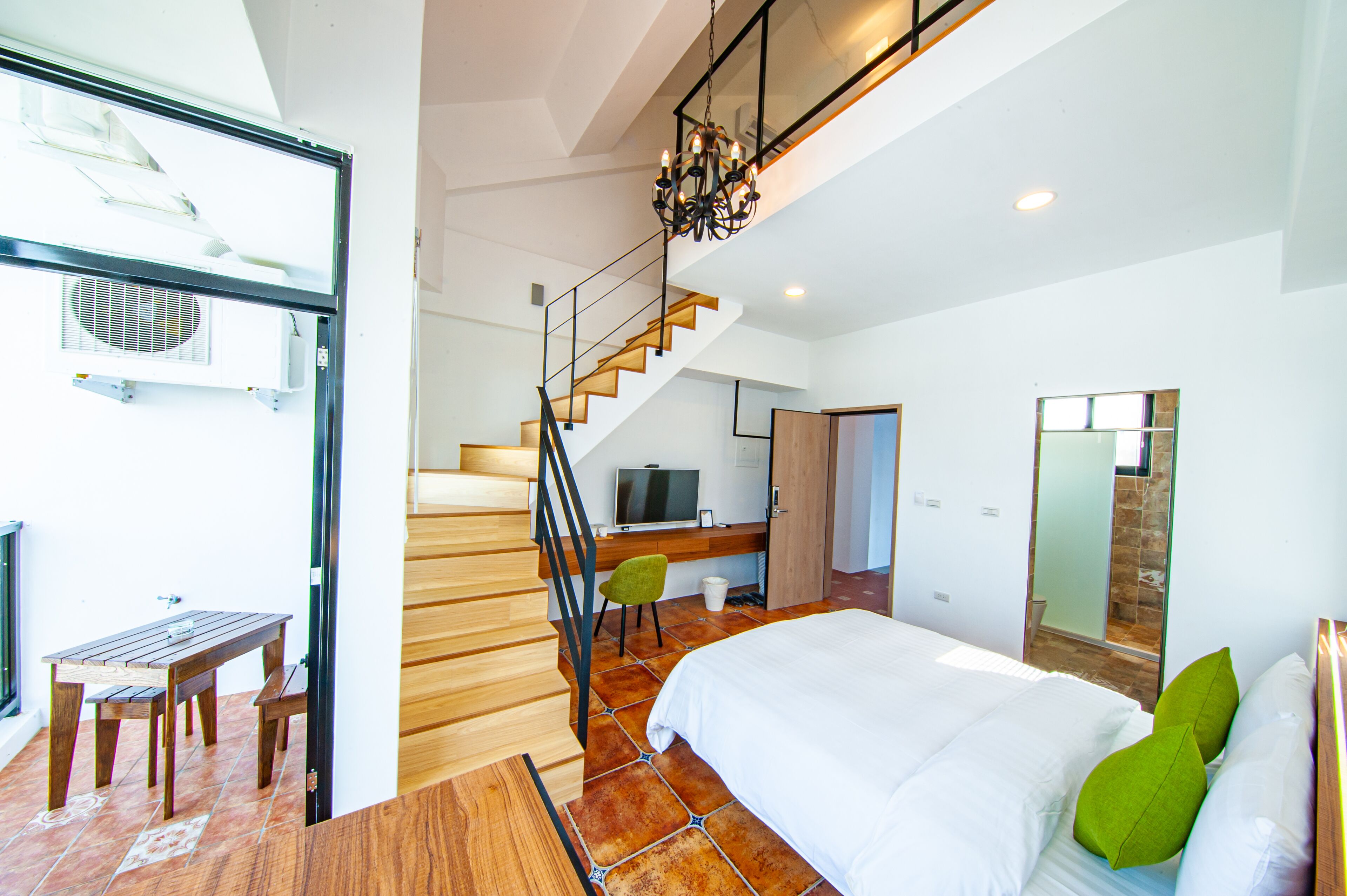 A modern bedroom with a large bed, a wooden staircase, and a TV in the corner.