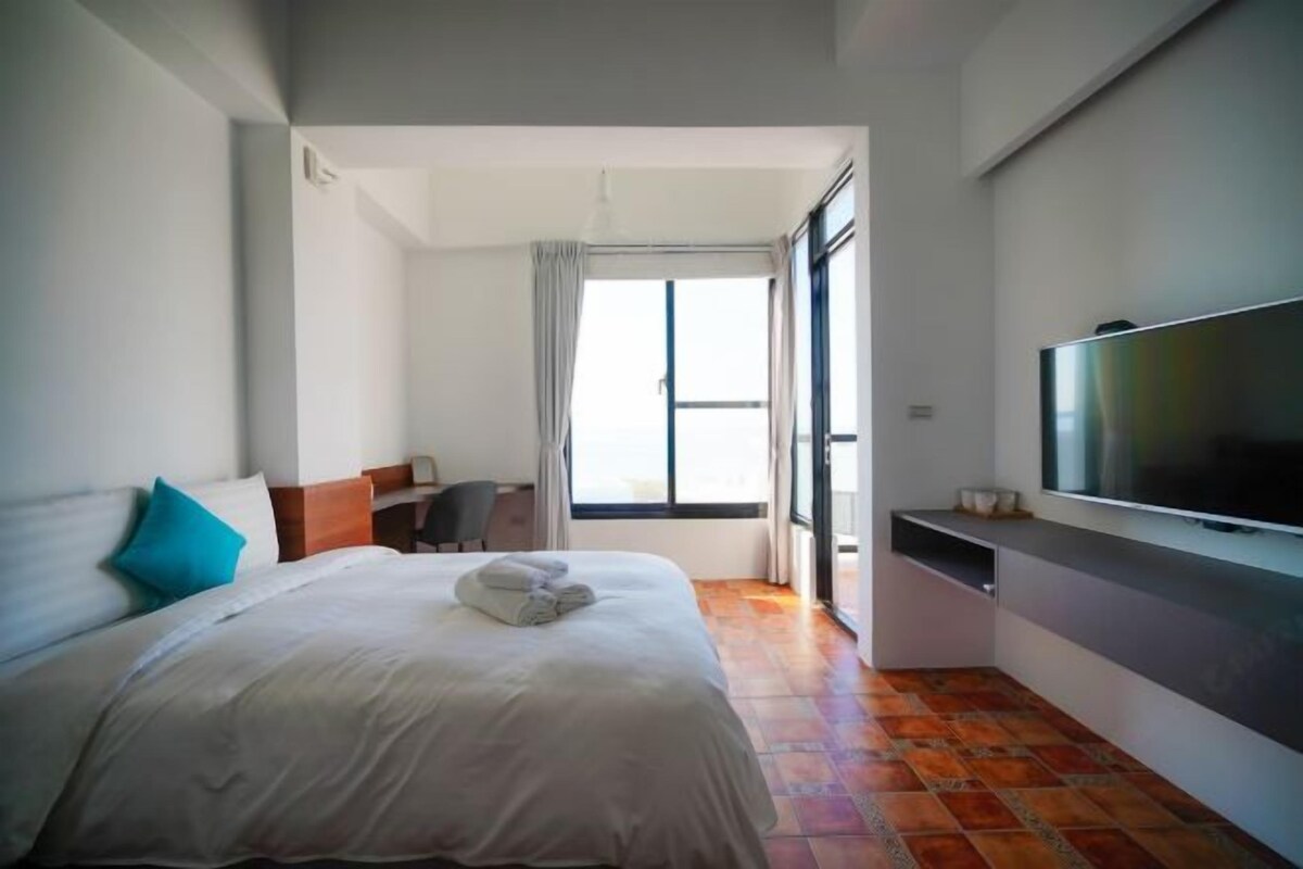 Una habitación de hotel con una cama, televisión, escritorio y ventana.