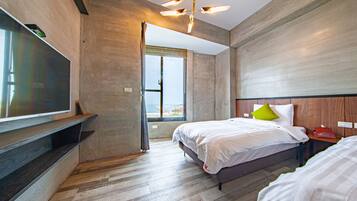 A modern hotel room with a large flat-screen TV mounted on the wall, a bed with white bedding and a green pillow, and a wooden headboard.