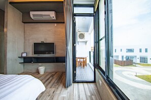 Una habitación de hotel con una cama, televisión, una mesita y ventana con vistas al exterior.