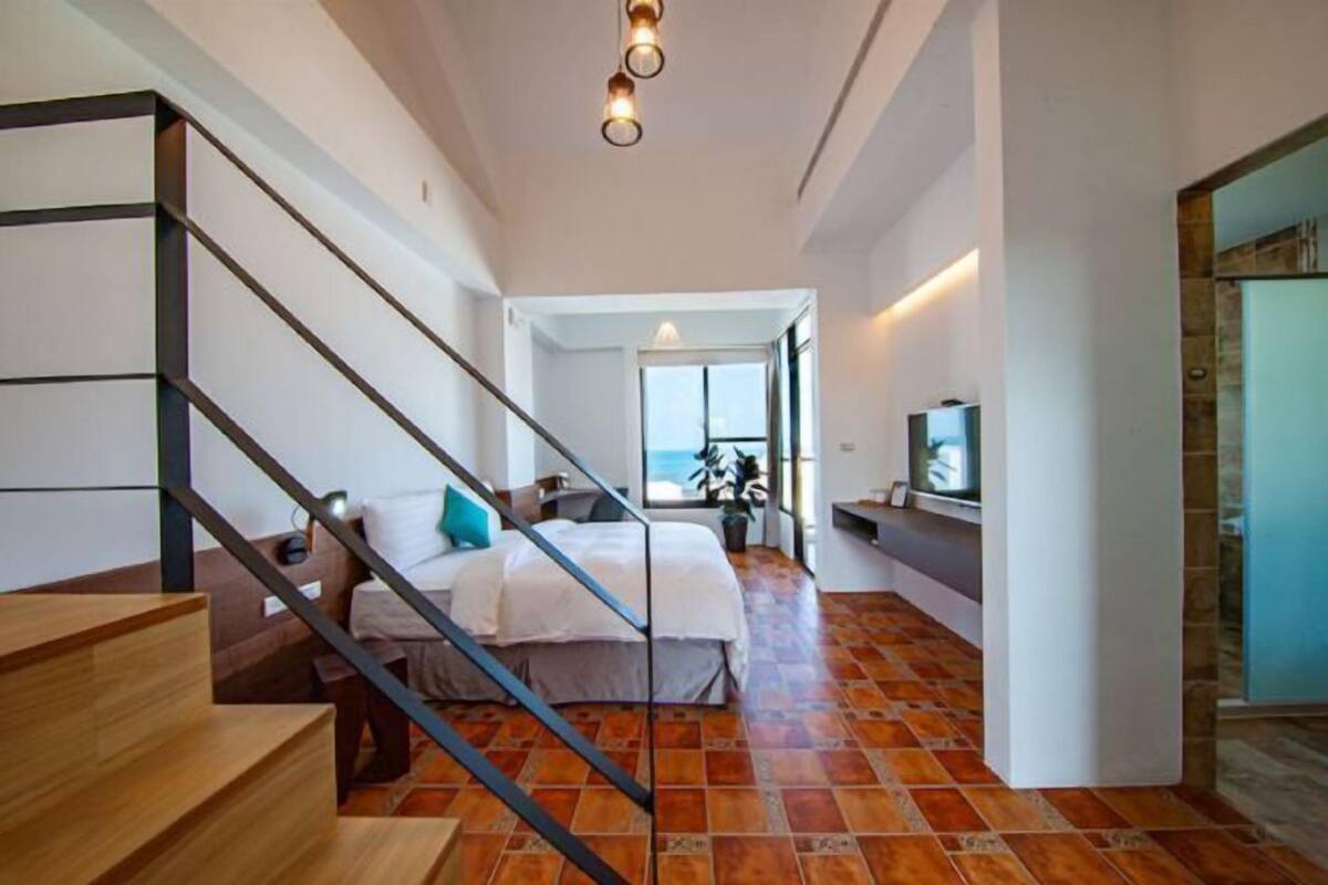 Ein Schlafzimmer mit Bett, Treppe, Fernseher und Blick ins Freie.