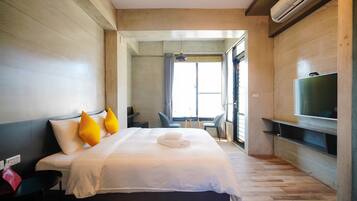 A modern hotel room with a large bed, a TV mounted on the wall, and a view of the outdoors through a window.