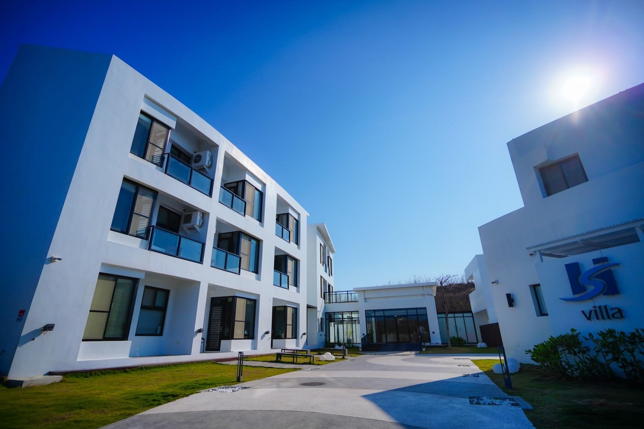 A modern villa with a white exterior, multiple balconies, and a clear sky.