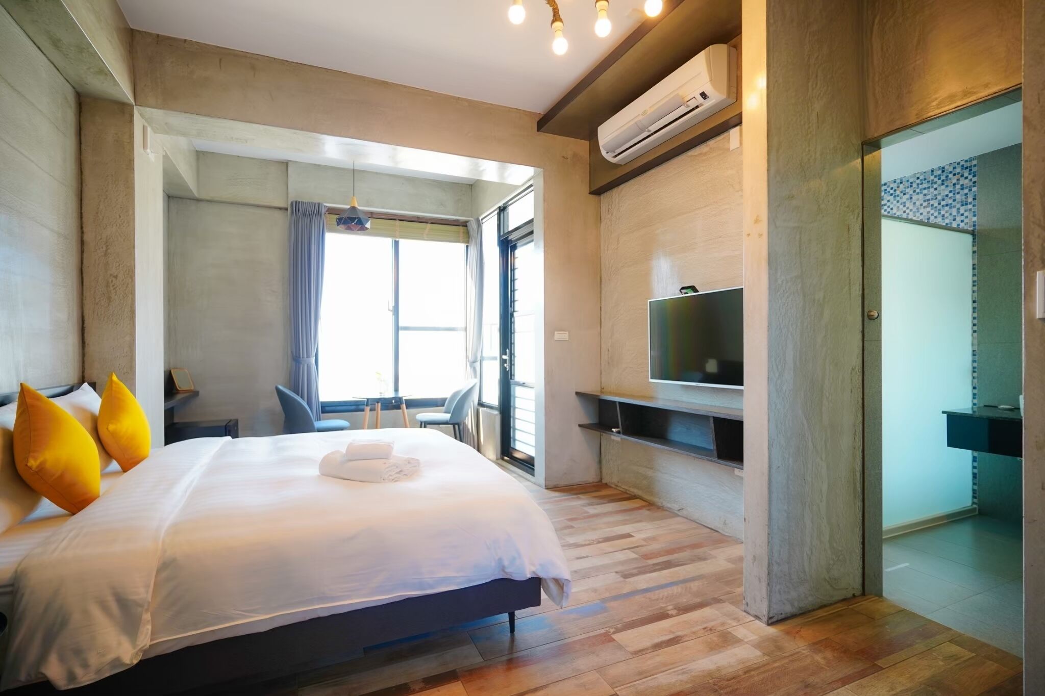A modern hotel room with a large bed, a TV, and a bathroom visible through an open door.