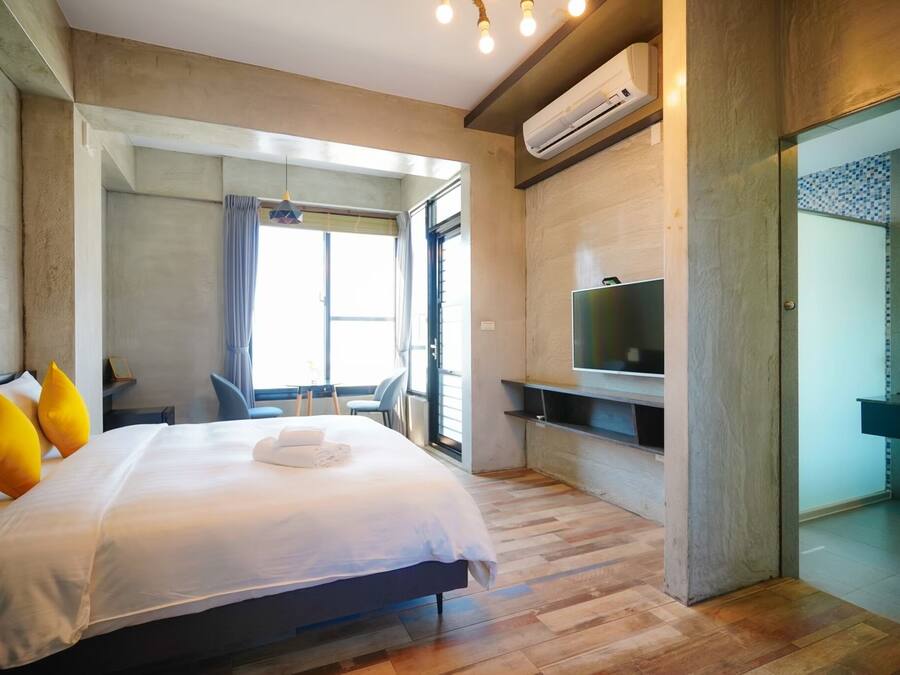 A modern hotel room with a large bed, a TV, and a bathroom visible through an open door.
