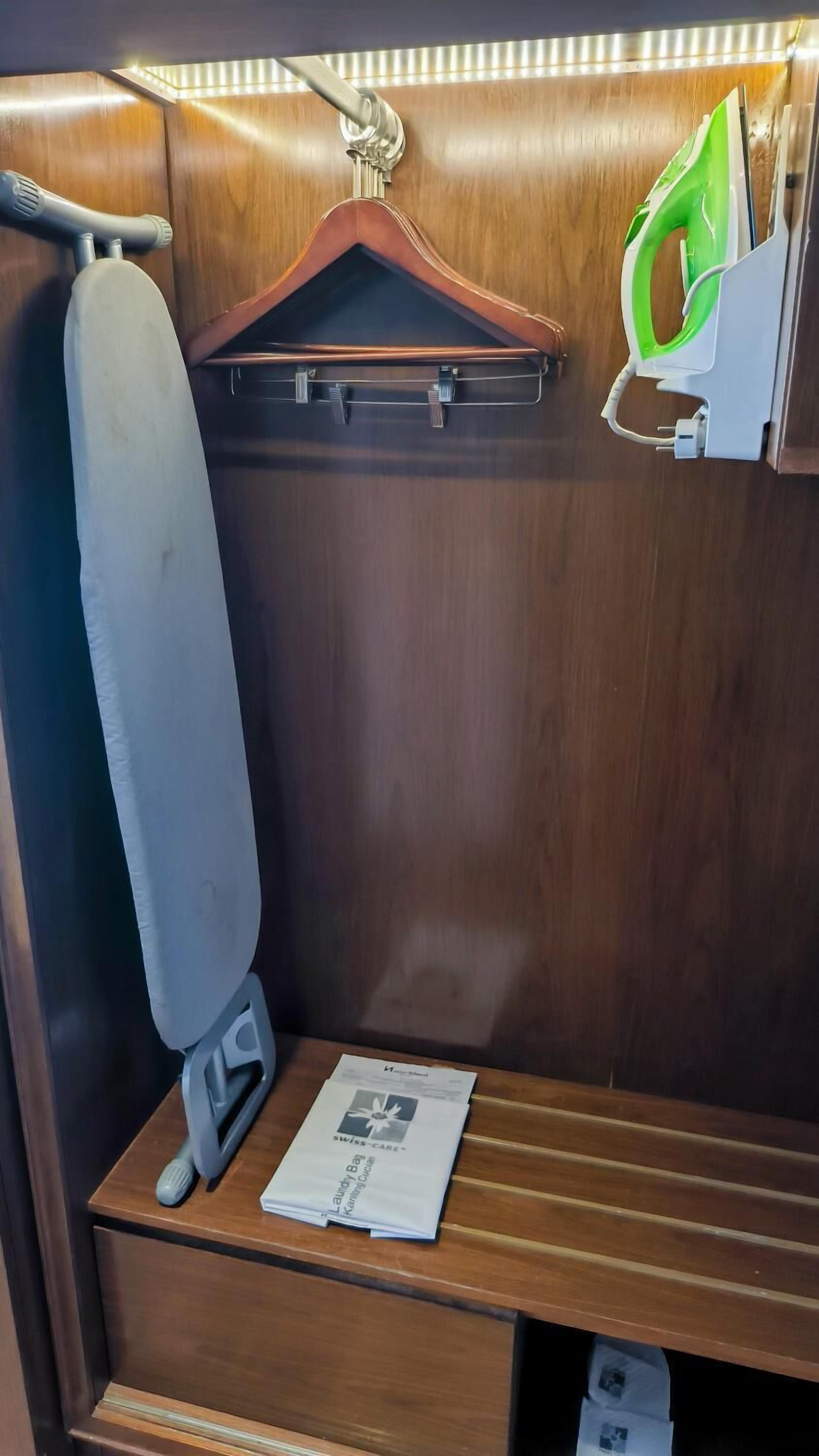 A compact, wooden interior with a hanging iron, a small ironing board, and a paper on the lower shelf.