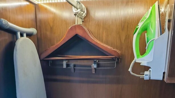 A compact, wooden interior with a hanging iron, a small ironing board, and a paper on the lower shelf. - Swiss-Belhotel Bogor (Bogor)