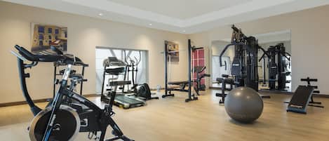 Egy tágas edzőterem kardioeszközökkel, súlyokkal és egy nagy méretű fitneszlabdával.