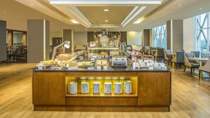 A buffet area with a variety of food items, a counter with plates, and a seating area with tables and chairs. - Swiss-Belhotel Bogor (Bogor)