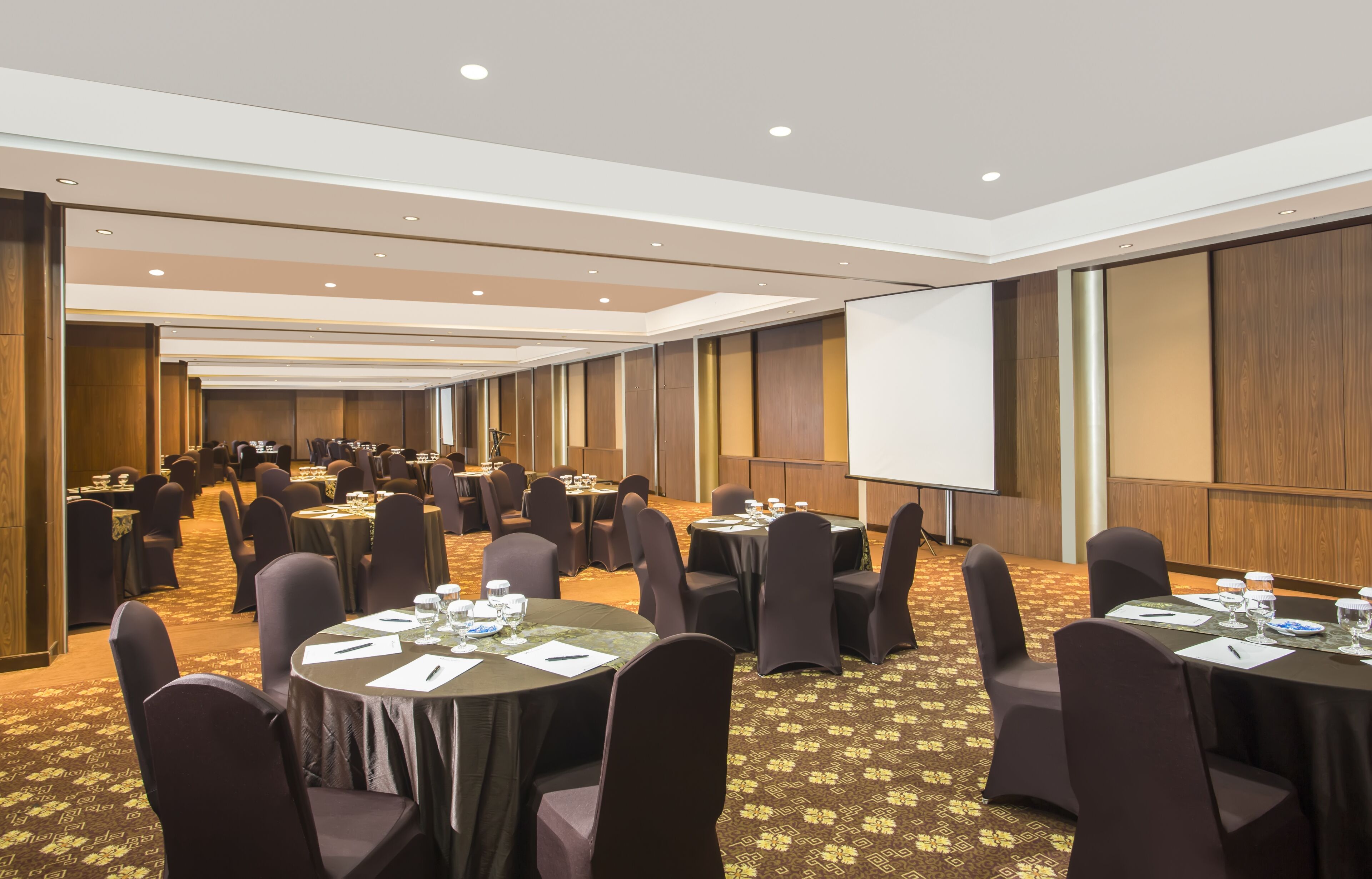 A conference room with multiple tables, chairs, and a projection screen.