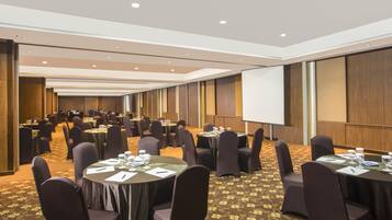 Un salón de conferencias con varias mesas, sillas y una pantalla de proyección.
