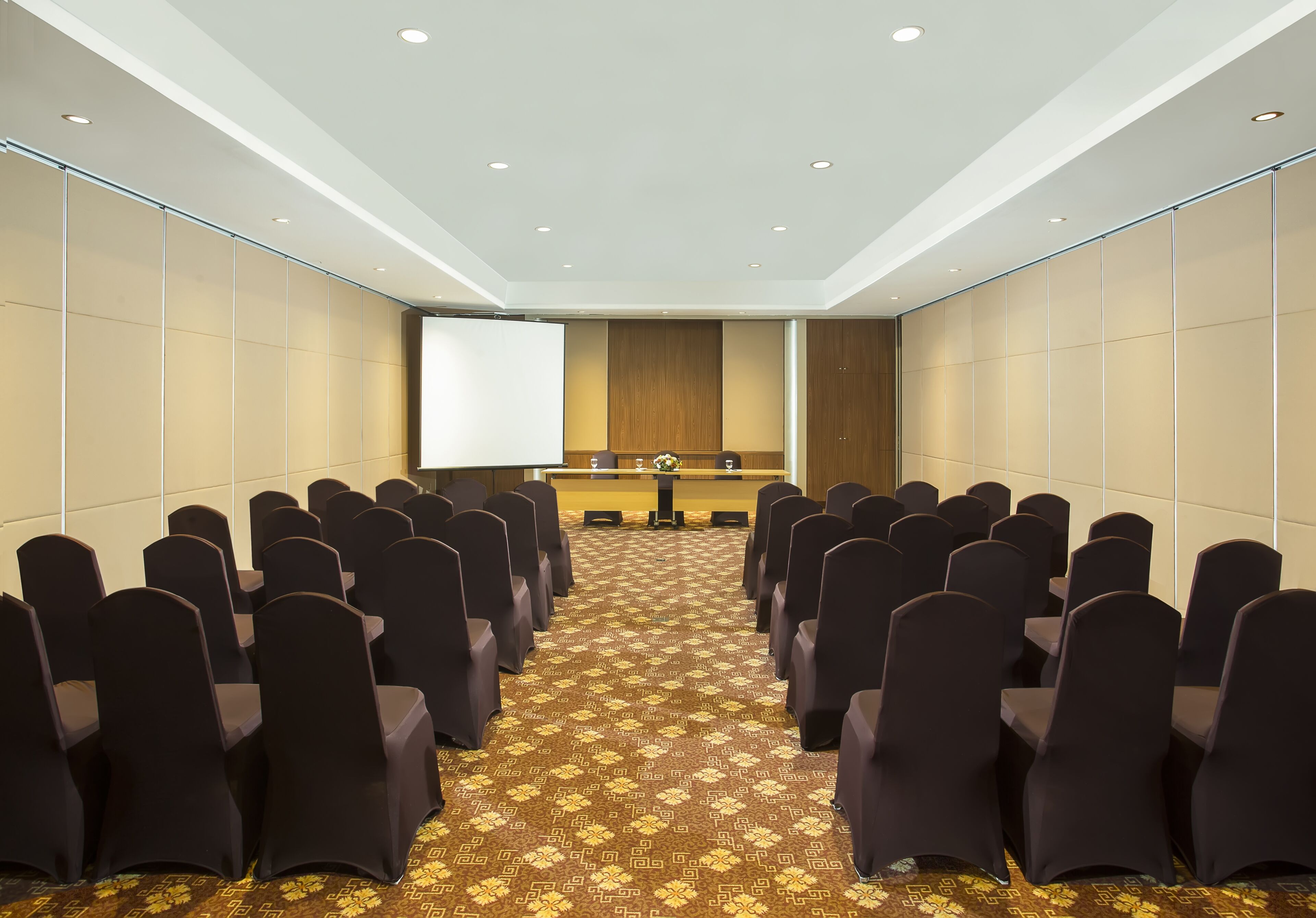 A conference room with rows of chairs, a podium, and a large screen at the front.