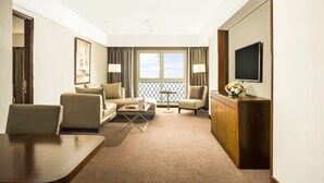 A hotel room with a sofa, armchairs, a small table, a TV, and a balcony with curtains. - Swiss-Belhotel Bogor (Bogor)