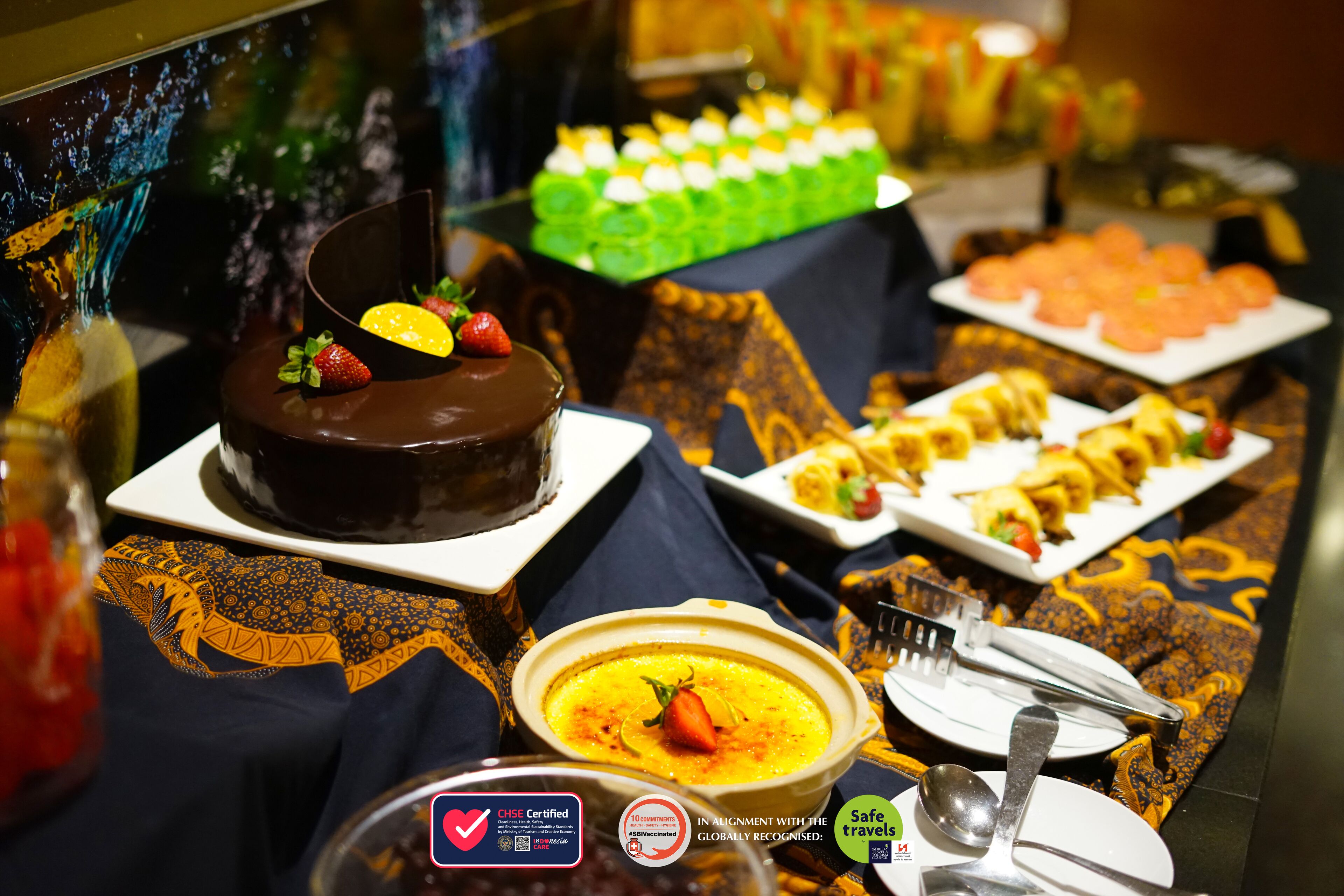 A buffet with various dishes, including a chocolate cake with strawberries, a green dessert tray, and a plate of pastries.