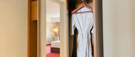 A hotel room with a wooden wardrobe, a hanging robe, and a bed with a red carpet.