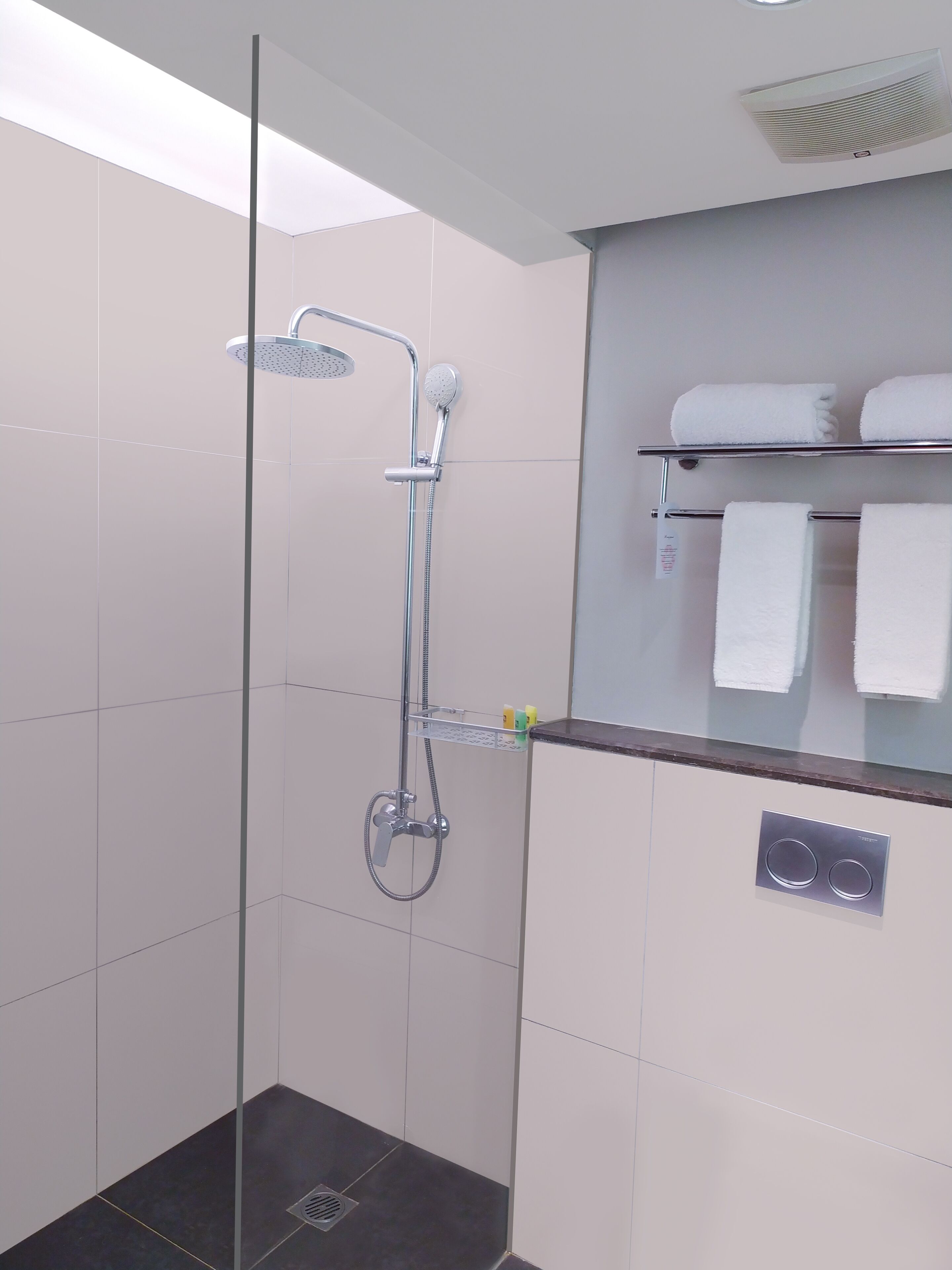 Una ducha moderna con puerta de vidrio, un perchero con dos toallas y un panel de control en la pared.