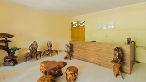 Un espace d’accueil avec un comptoir de réception en bois, un mur jaune et plusieurs sculptures en bois originales.