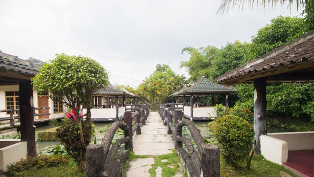 Un sentier mène à des pavillons de style traditionnel, entourés d’une végétation luxuriante.