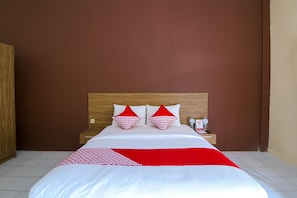 Ein Hotelzimmer mit einem hölzernen Kopfteil, einem großen Bett mit weißer und roter Bettwäsche sowie einem Nachttisch mit einer Flasche und einer Fernbedienung.
