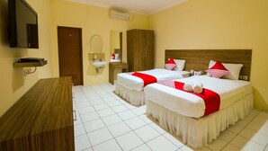 Une chambre d’hôtel avec deux lits, un bureau en bois, une télévision et une salle de bain équipée d’un miroir et d’un lavabo.