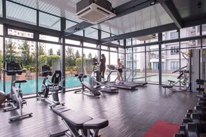 Un gimnasio moderno con amplias ventanas, diverso equipo de ejercicio y vistas a una piscina.