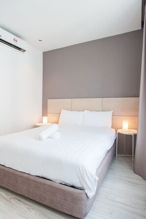 Una cama bien hecha con sábanas blancas, cabecera de madera y dos lámparas de noche.
