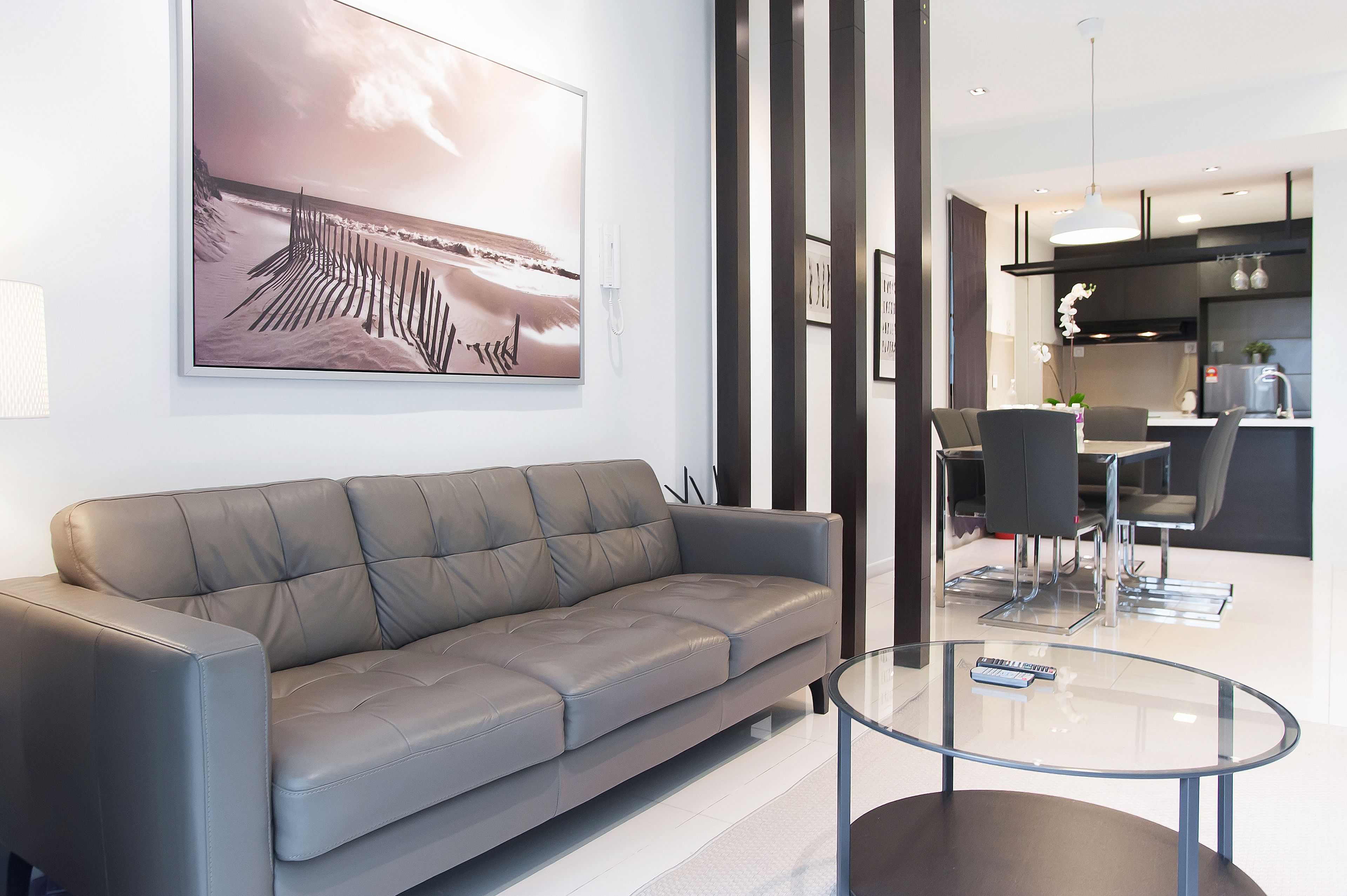 A modern living room with a grey sofa, a glass coffee table, and a large abstract painting on the wall.