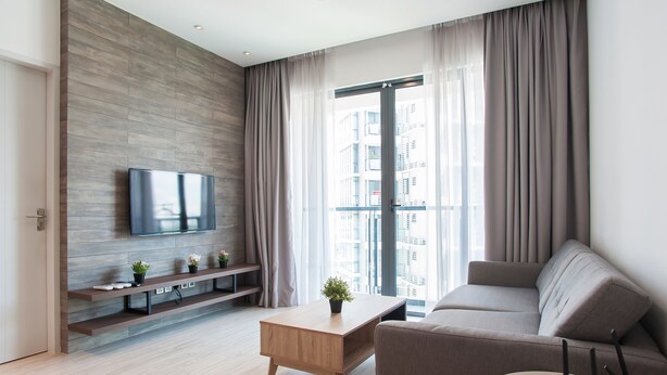 A modern living room with a flat-screen TV mounted on a wooden wall, a sofa, a coffee table, and a window with curtains. - Boulevard Residence (Petaling Jaya)