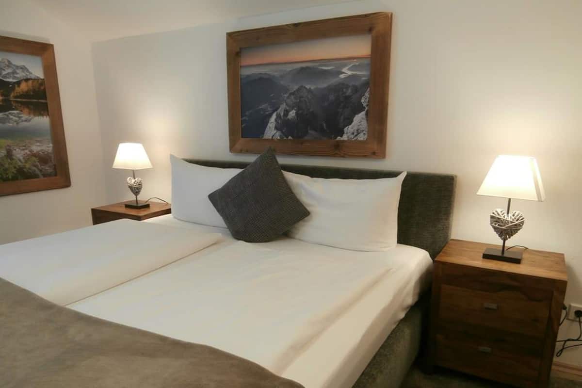 A neatly made bed with a pillow, two bedside tables with lamps, and two framed pictures on the wall.