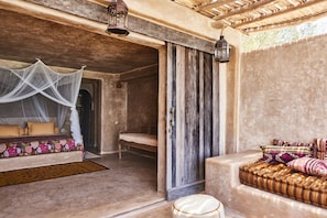 A room with a bed, a bench, a cushioned seating area, and a door leading to another room.