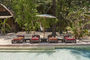 A poolside area with lounge chairs and a table, surrounded by tropical vegetation.